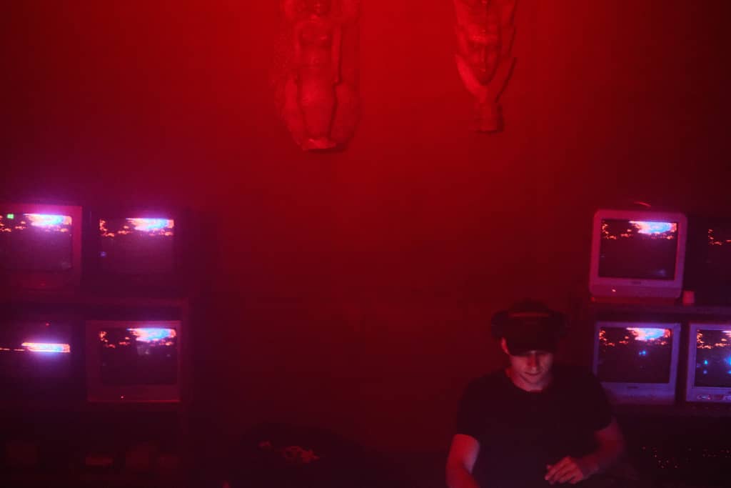 Hilda Hilda with TVs and two tribal statues on the wall, red lights